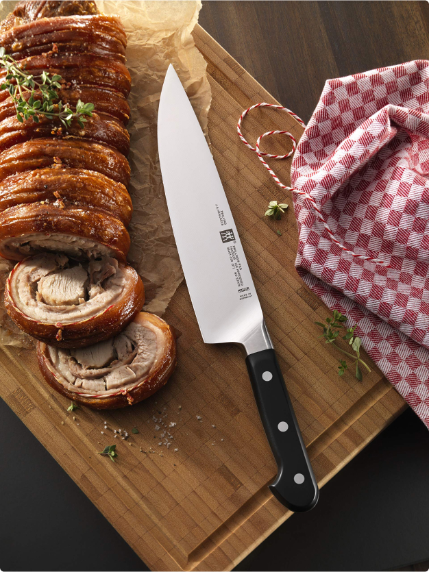 Rotolo di carne farcito affettato su tagliere di legno con coltello e tovaglietta rossa a quadri, dettagli rustici e aromi di erbe.