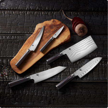 Coltelli da cucina affilati su tagliere in legno, con impugnature nere, sfondo scuro a piastrelle ricercate.