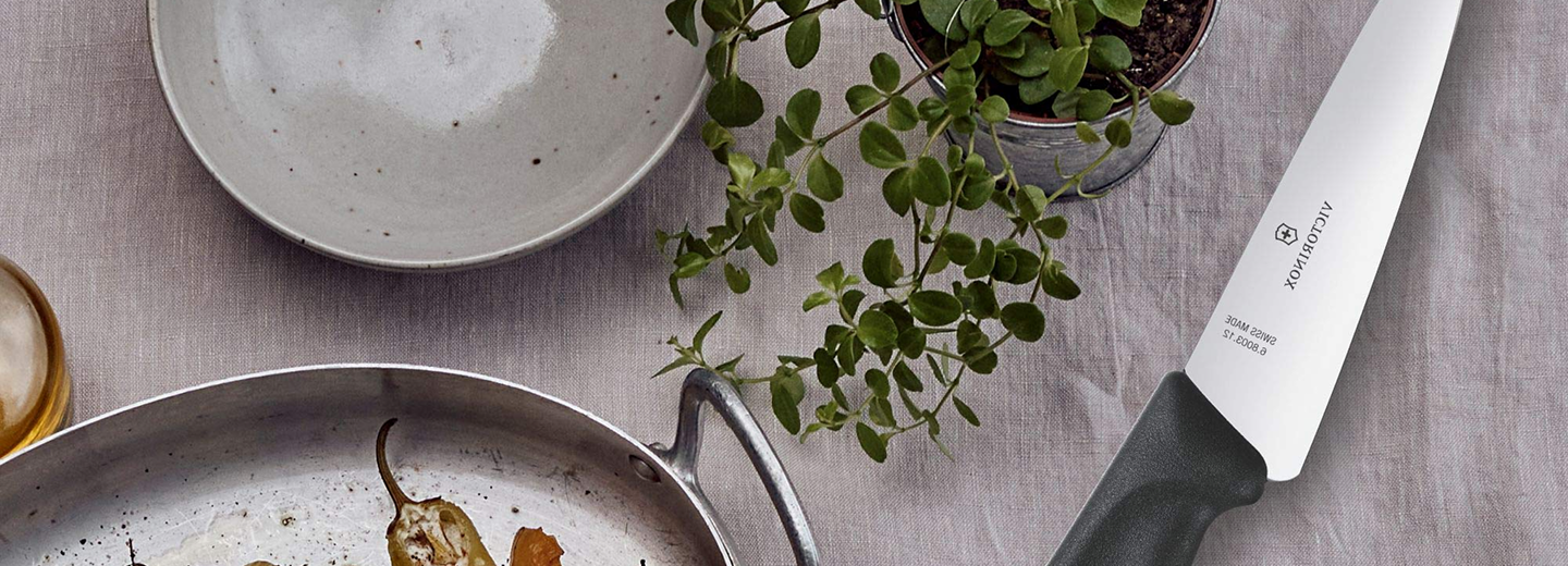 Piatto bianco, pianta verde in vaso e padella antiaderente su tovaglia chiara, scena luminosa e minimalista.